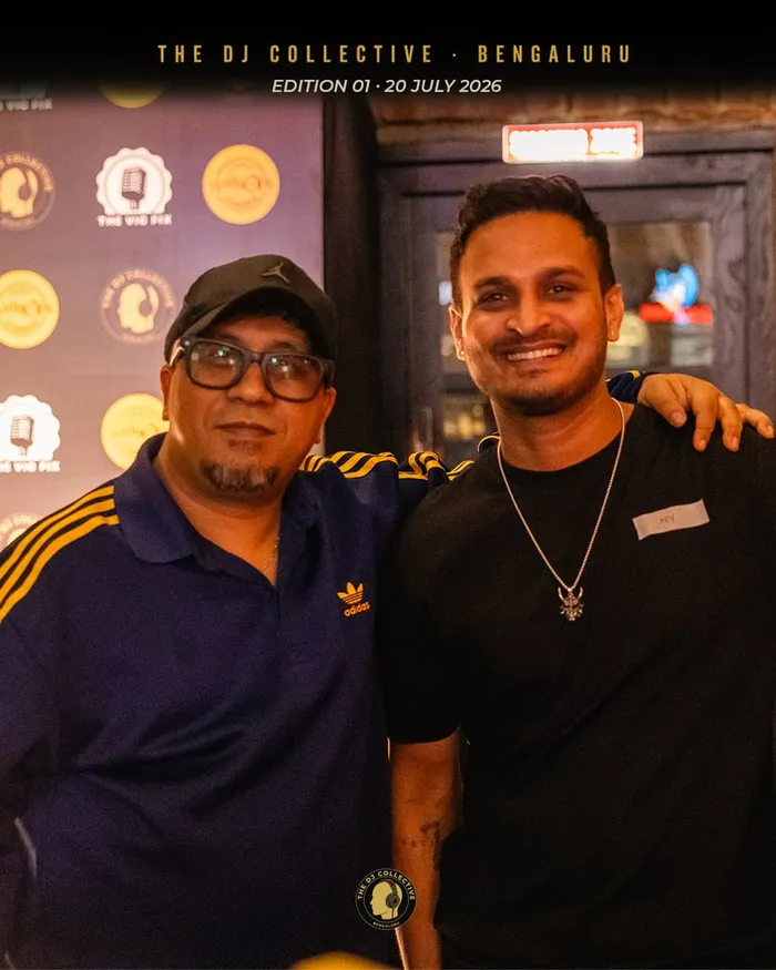 Two DJs posing together in front of the backdrop, arms round each other