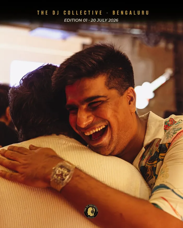 Two DJs in a long hug, one grinning over the other's shoulder