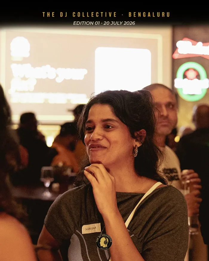 A DJ smiling in the crowd, the screen glowing behind